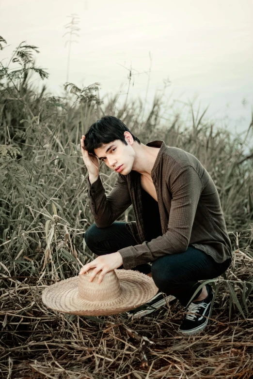 a young man in a field with his hands on his hat