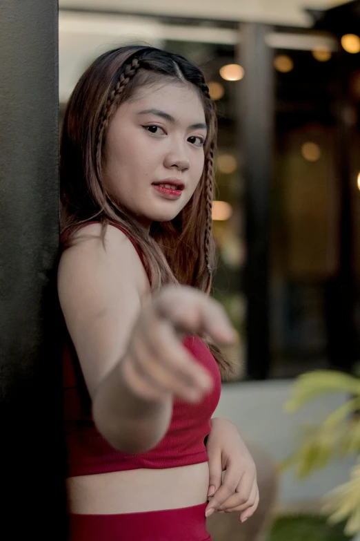 a girl in a red shirt leaning on a pole pointing