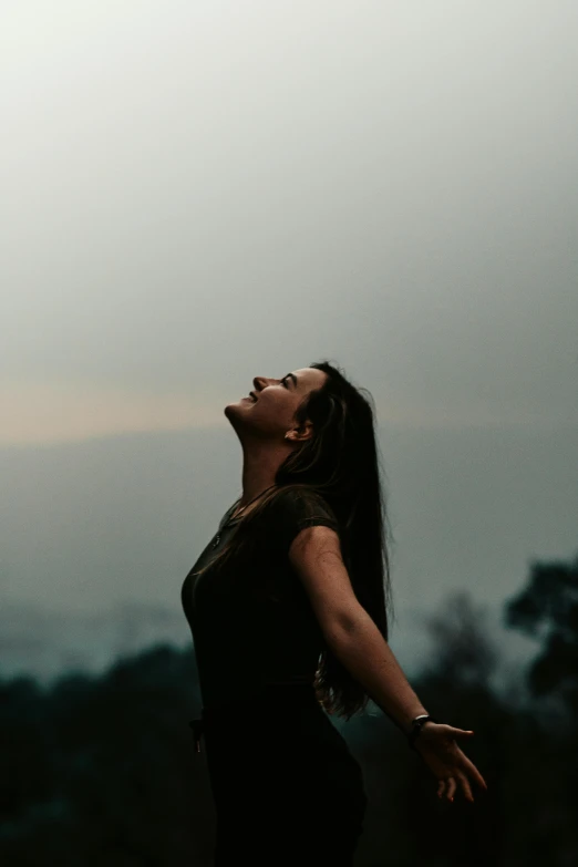 a woman with dark hair stands in the field as a bird flies by