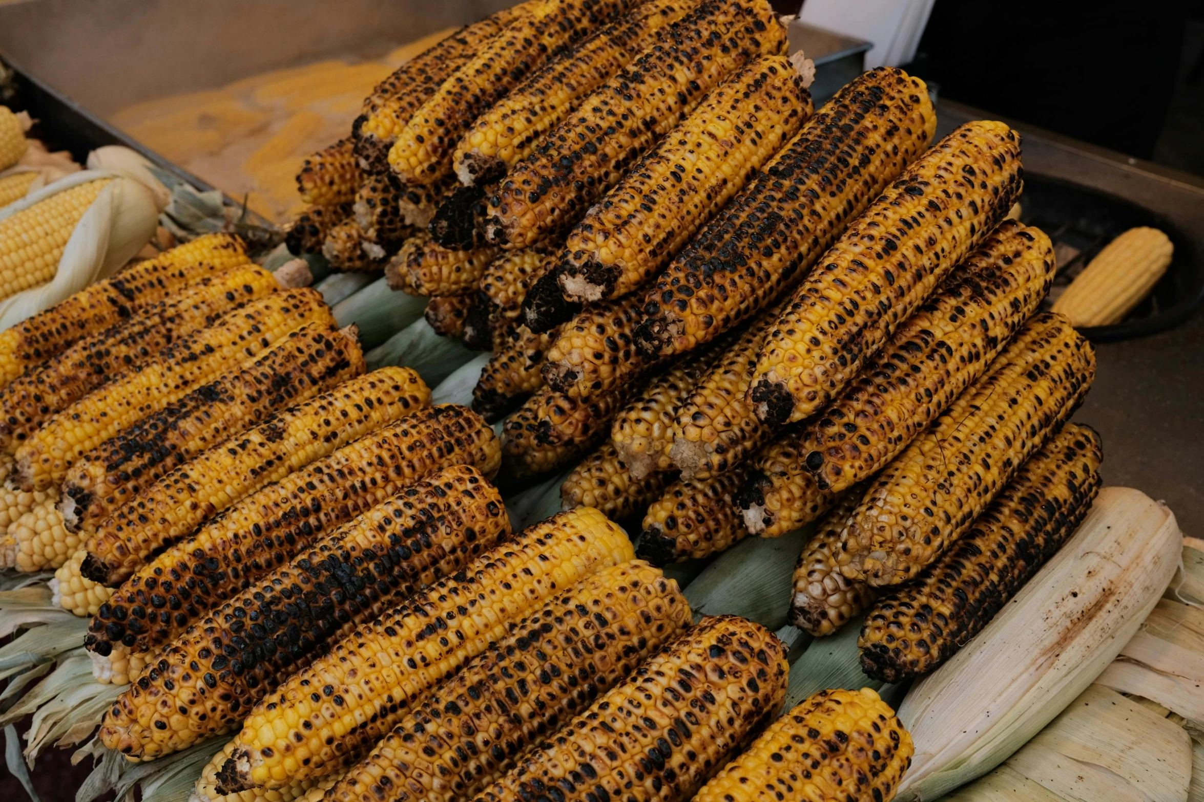 a group of grilled corn on the cob with other corn kernels arranged on the side