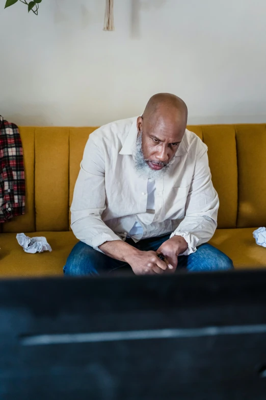 a man sitting on a yellow couch with his hands in his pockets