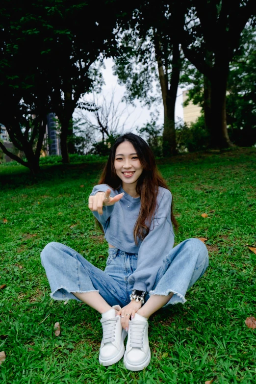 a woman with long hair sitting on the grass pointing to soing