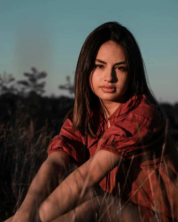 a woman sitting down in a field, and wearing an orange shirt