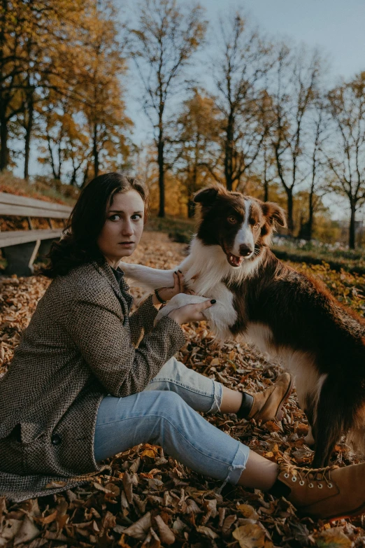 a girl sitting in the leaves with a dog