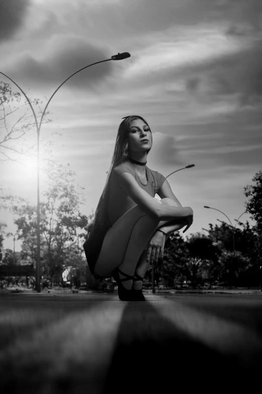 woman with long hair squatting on pavement near street lamps