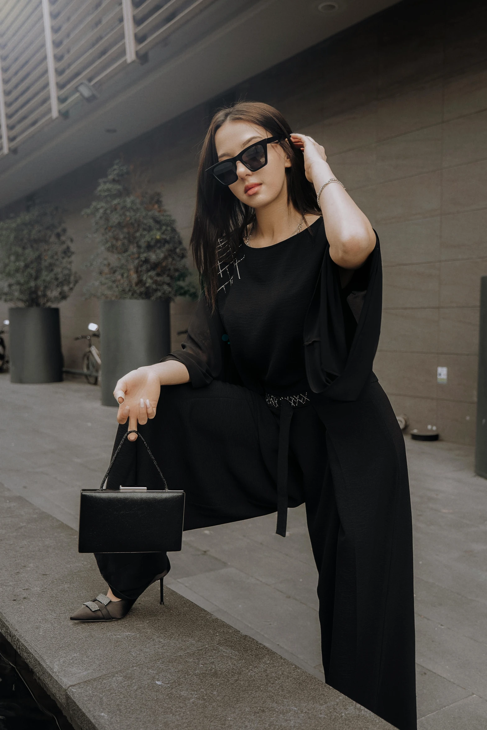 woman sitting on ledge in front of building wearing black outfit and sunglasses