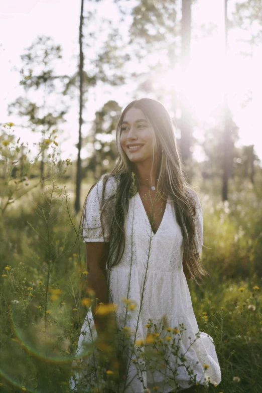 a woman is standing in a field with sun beaming through the trees