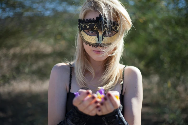 a beautiful blond woman in a black top with a carnival mask on