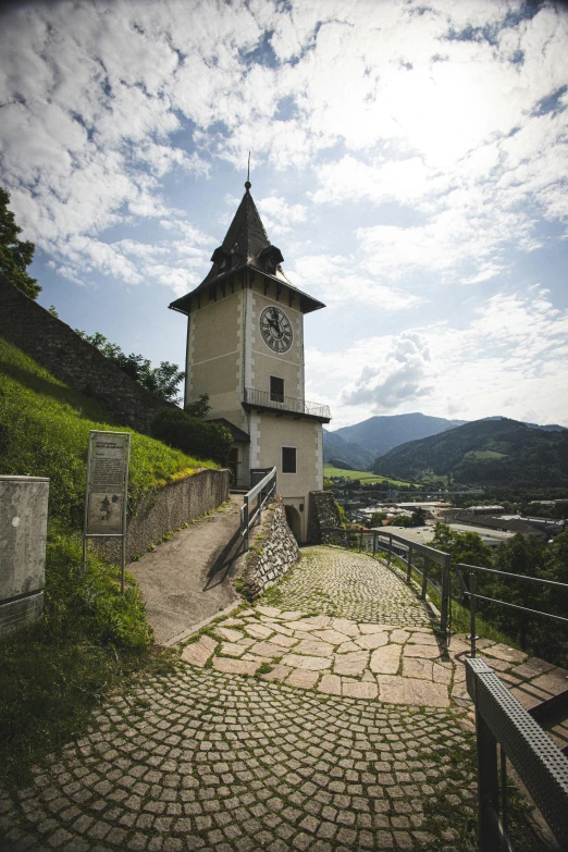 a clock tower with a path leading to it and mountains in the background