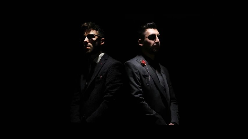 two men in black suits with dark background