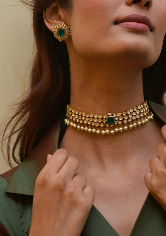 a woman with gold jewelry wearing an emerald stone choket