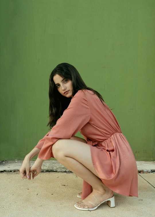 a woman posing in a pink dress next to a green wall