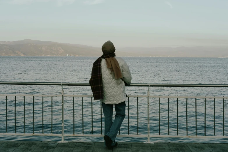 man walking along side a metal railing by the ocean