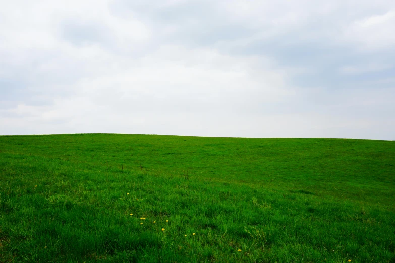 an empty grassy hill under a cloudy sky