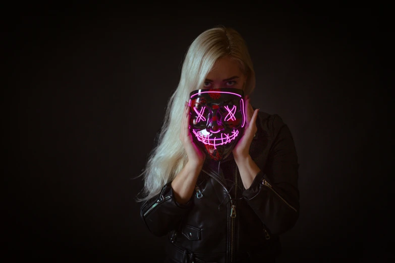 a woman wearing a neon mask holds her face to the camera