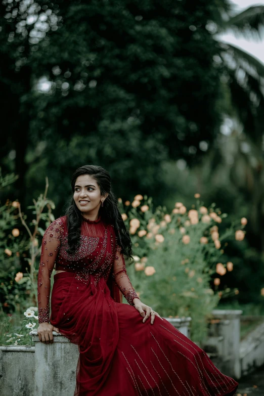 a woman in a red dress sits in front of trees