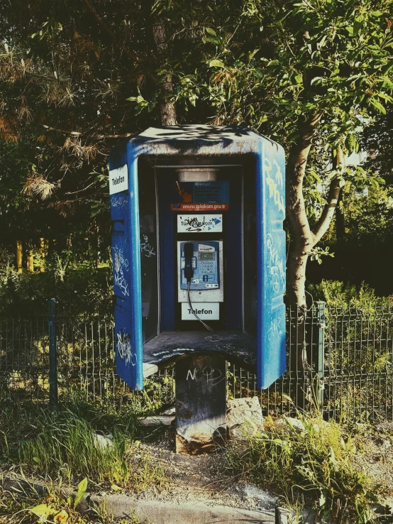 a public phone booth near trees and fence