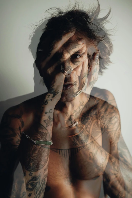 the man with tattoos covers his face by covering his hands to face with his nose