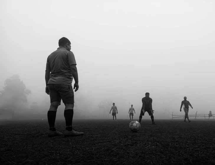 several players of different ages playing soccer on a foggy day