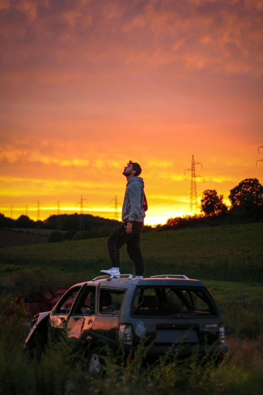 man standing on top of a vehicle at sunset