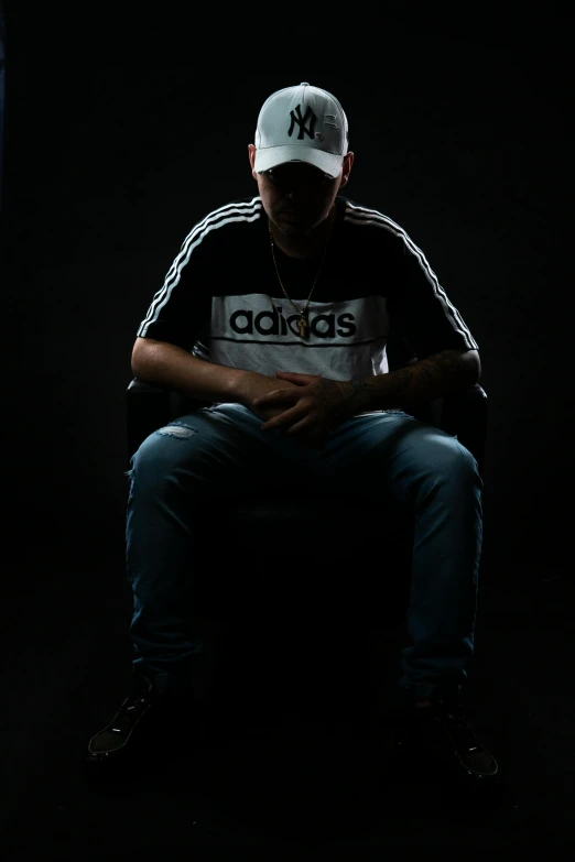 a man sits in the shadows while wearing a cap