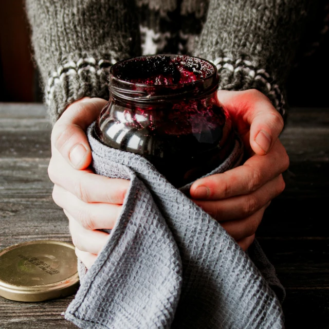 a person's hand holding a jar of red liquid