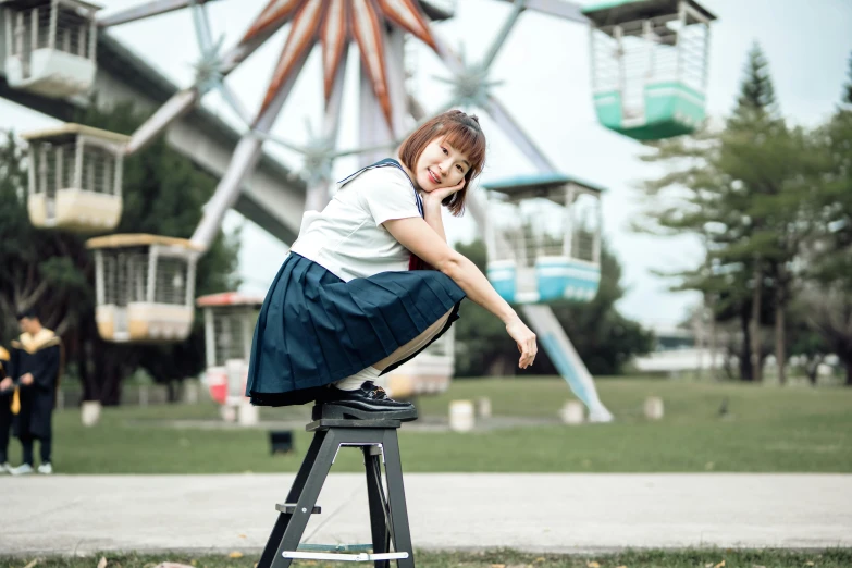 a woman posing on top of a stool with a ferris wheel in the background