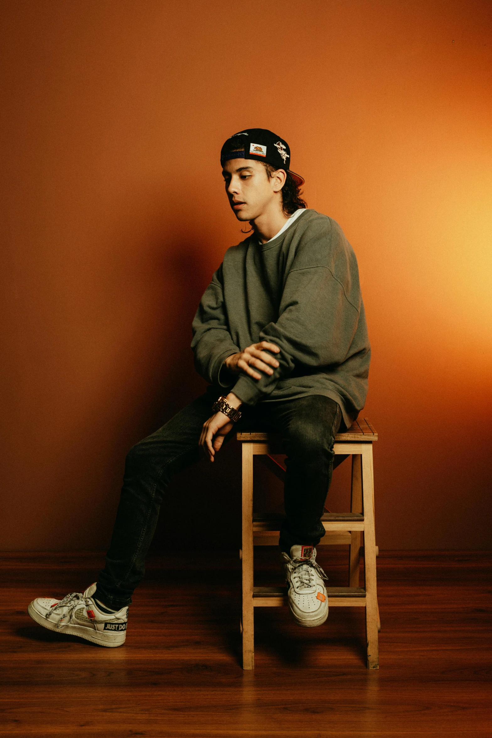 a person wearing a cap sits on a stool with his hands behind their back