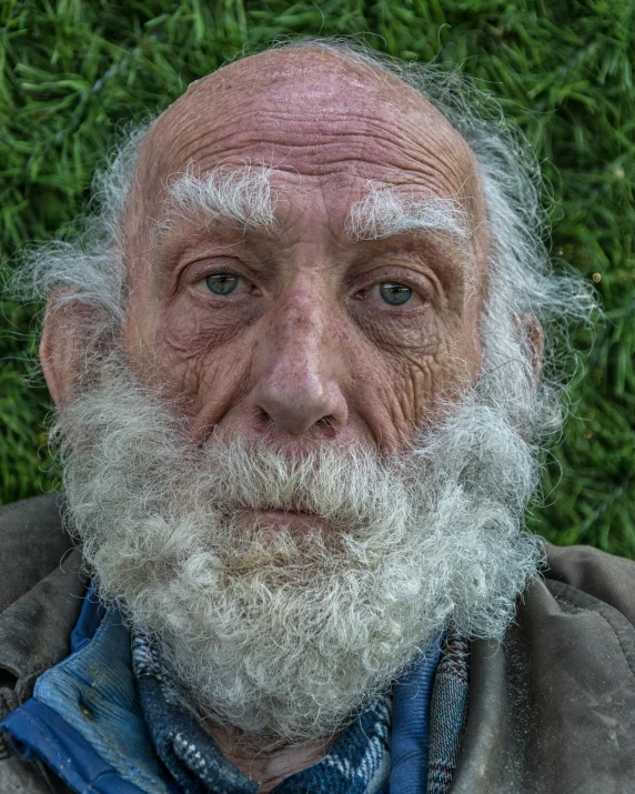 a man with white hair, a beard and beard ring looks into the camera