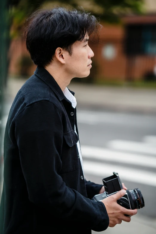 a man with dark hair and wearing a black jacket carrying a camera