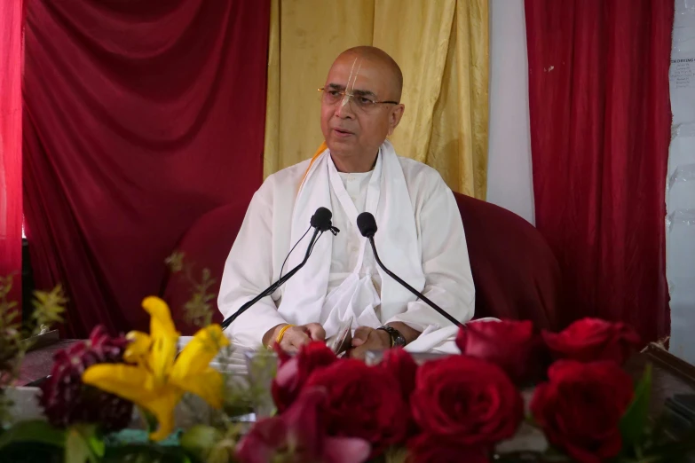 a man in white is sitting at a table with a microphone