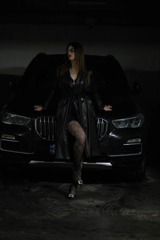 a woman is leaning on the front end of a black car