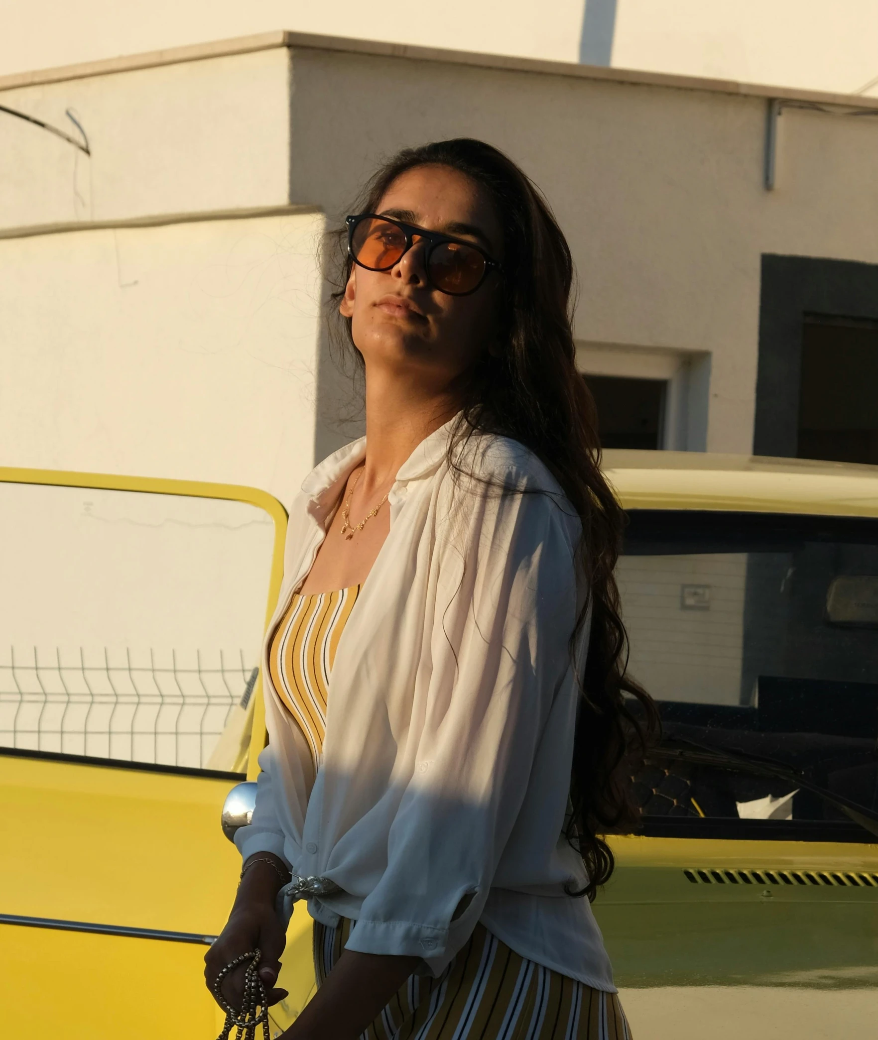 young woman wearing sunglasses standing next to a yellow vintage car