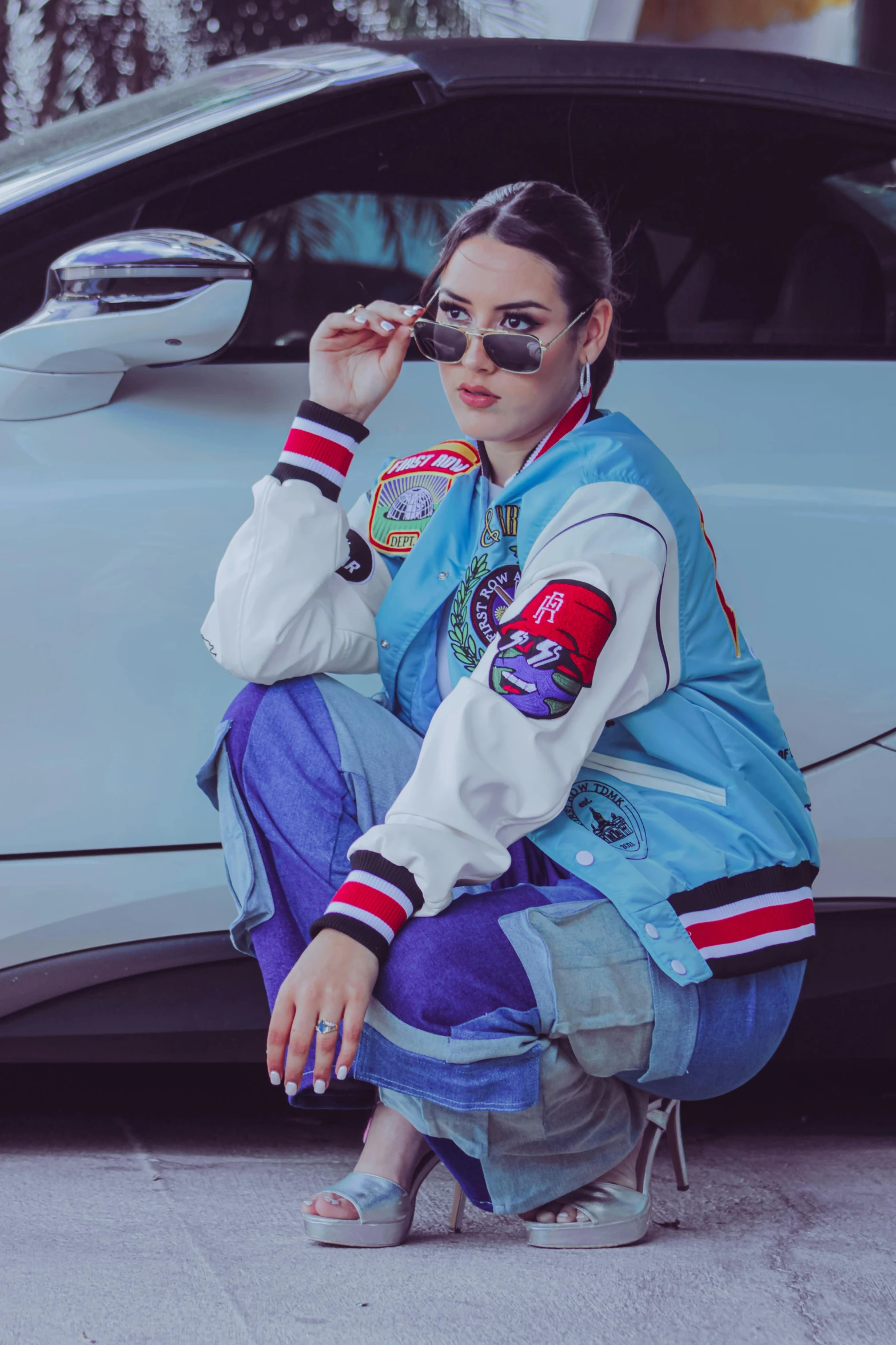 a woman wearing a jacket and sunglasses sitting in front of a car