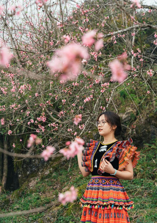 young asian woman in a colorful dress standing next to blooming tree