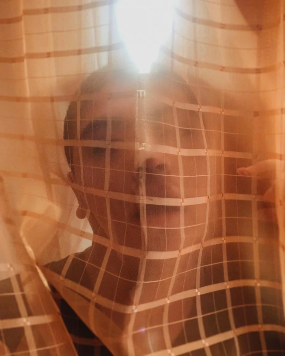 a man behind a sheer curtain in front of a window