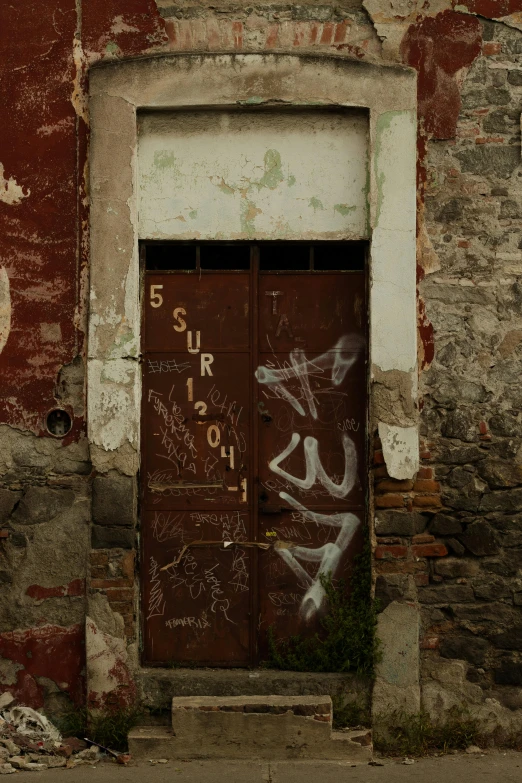 a rusty door with graffiti on the side of a old wall