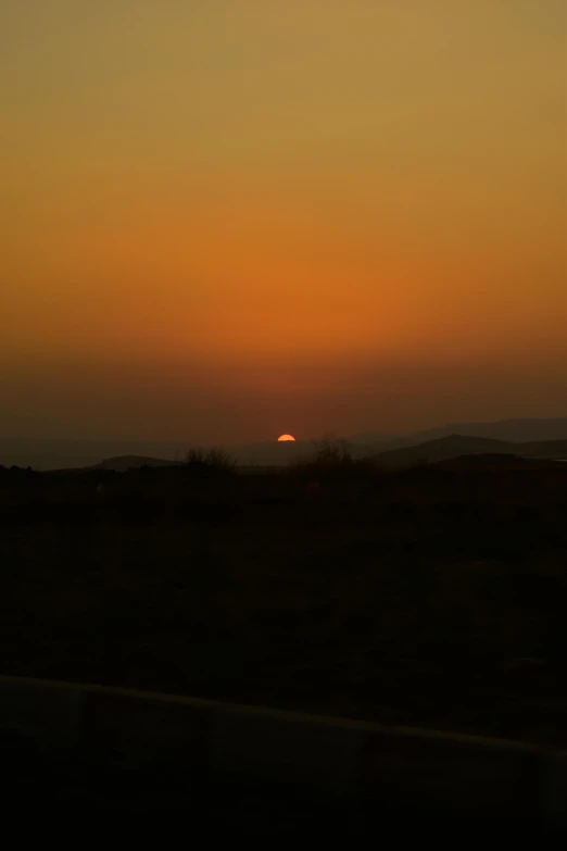 the sun sets on the horizon near a hill