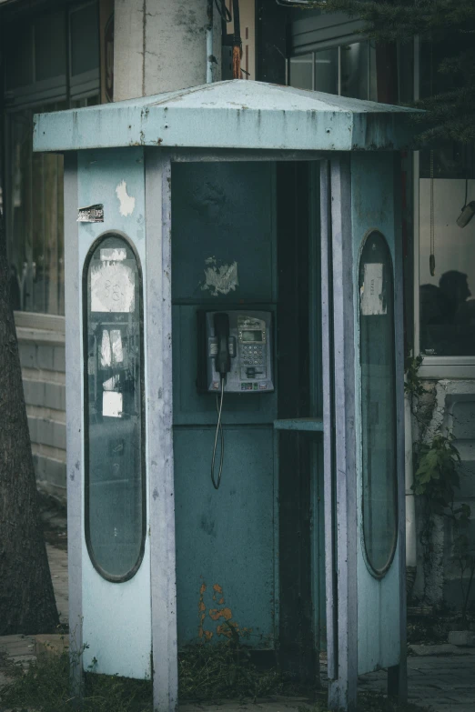 old telephone box on a side walk near a tree