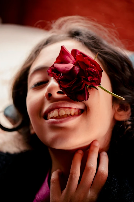 the girl smiles while holding a rose in her mouth