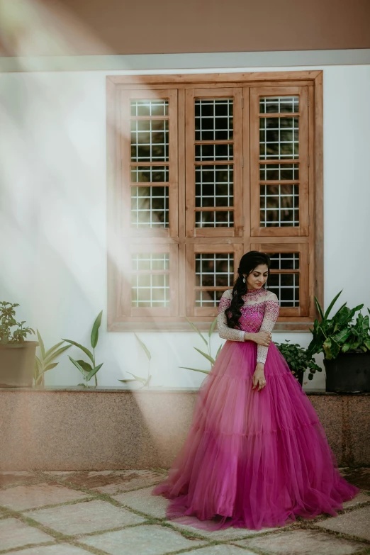 a woman stands in front of a window with a pink dress