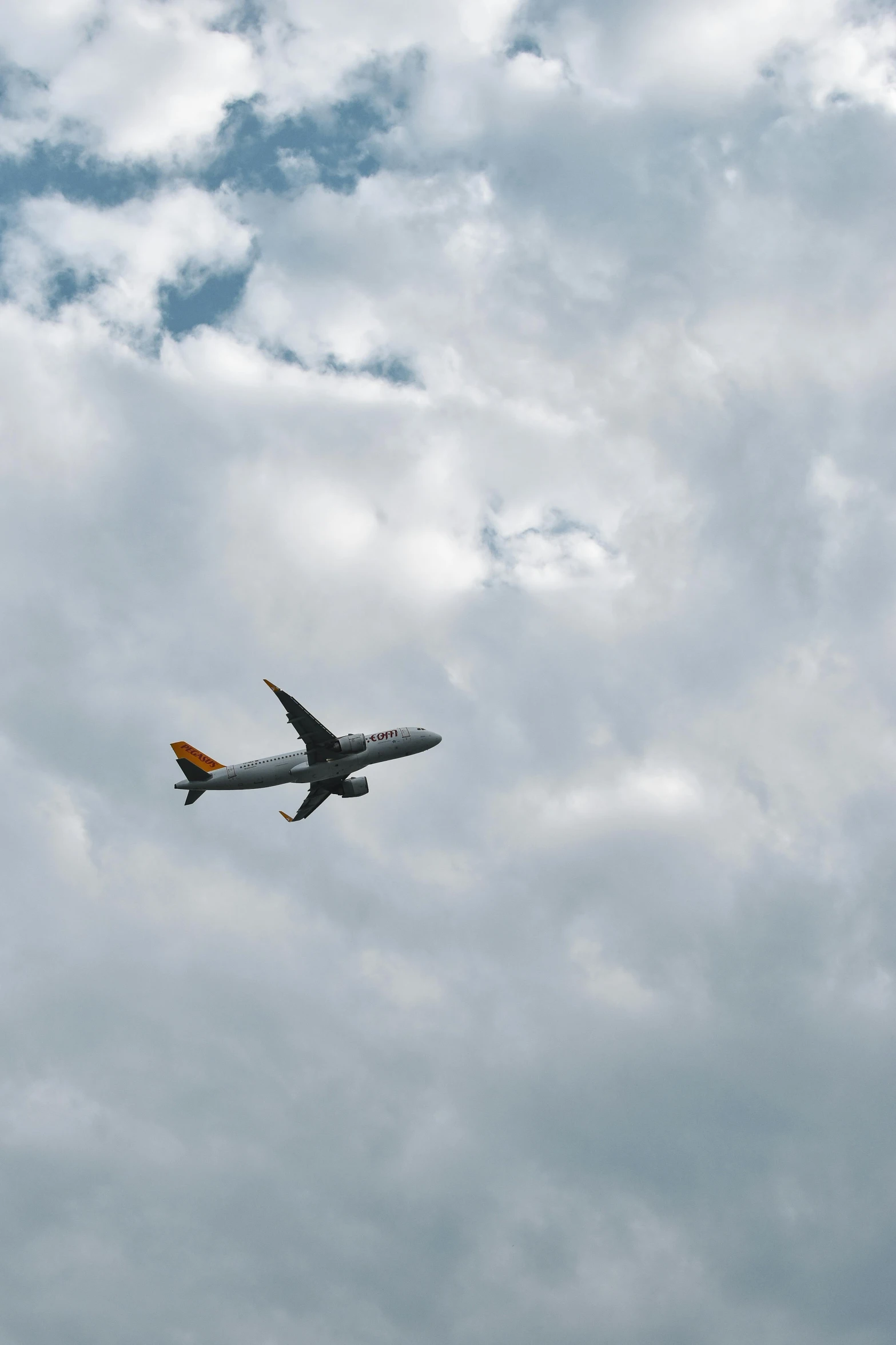 an airplane flies against a grey and cloudy sky