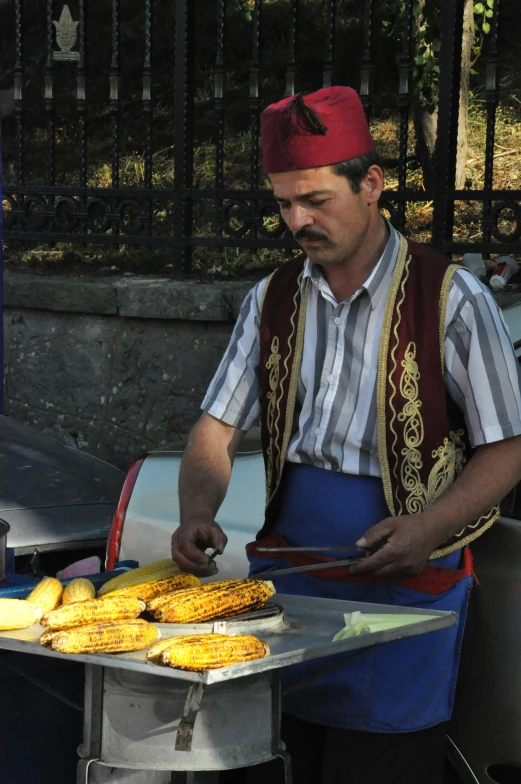 a man in striped shirt and apron slicing corn on grill