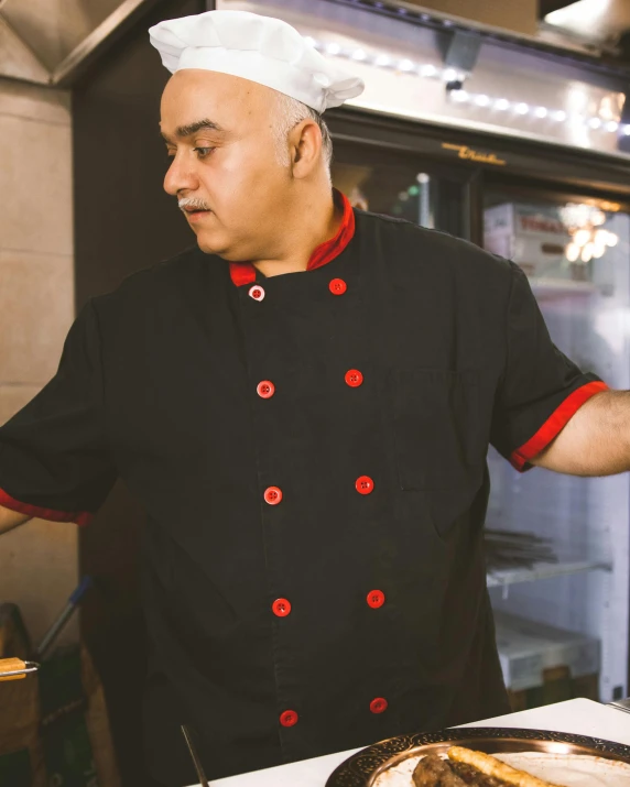 a chef with a red on his jacket stands at the ready plate