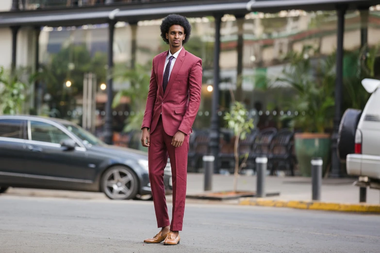 a man in a red suit and brown sandals stands on a street