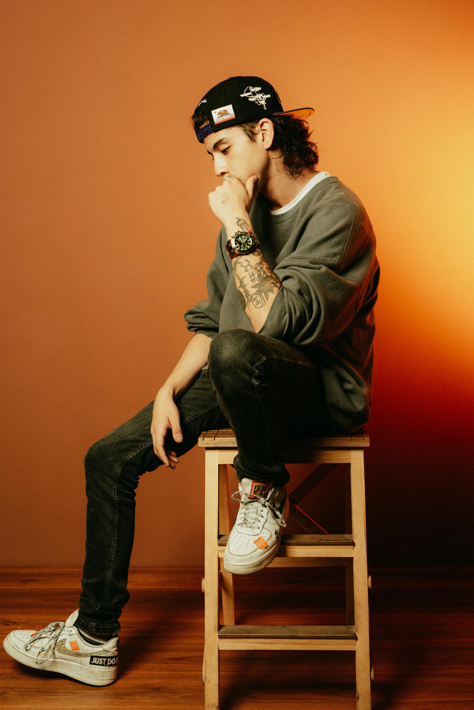 the young man is sitting on a stool wearing a cap