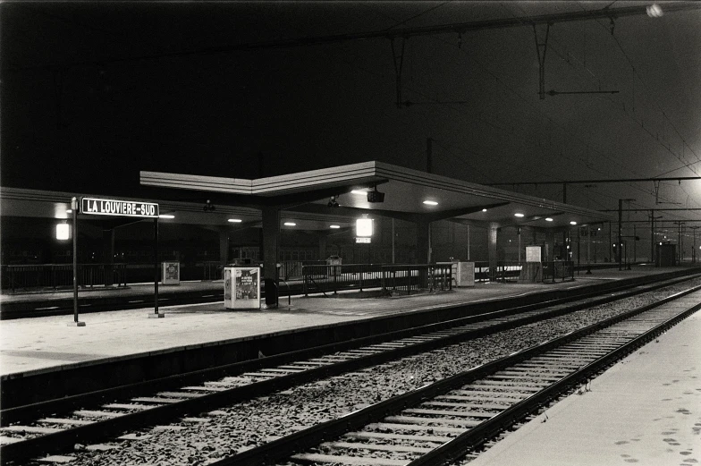 black and white pograph of train tracks in a station at night