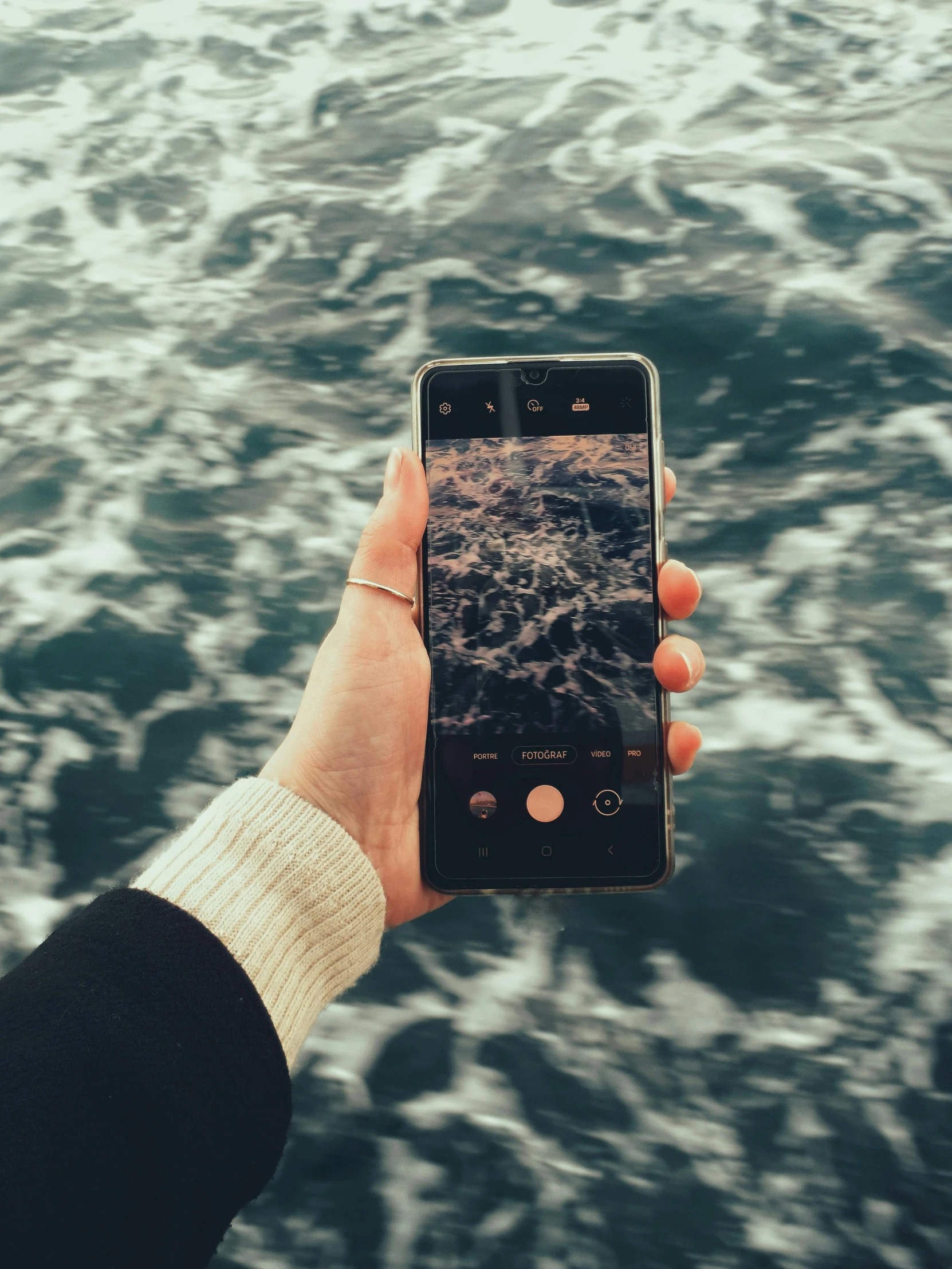 hand holding phone showing camera on surface with ocean