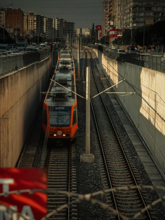 a orange train traveling down tracks next to tall buildings