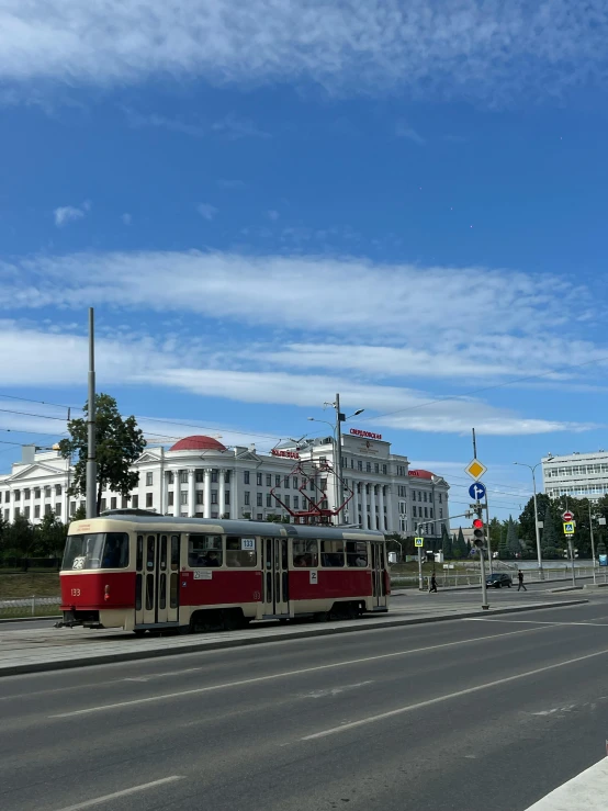 a trolley traveling down the street next to a large white building